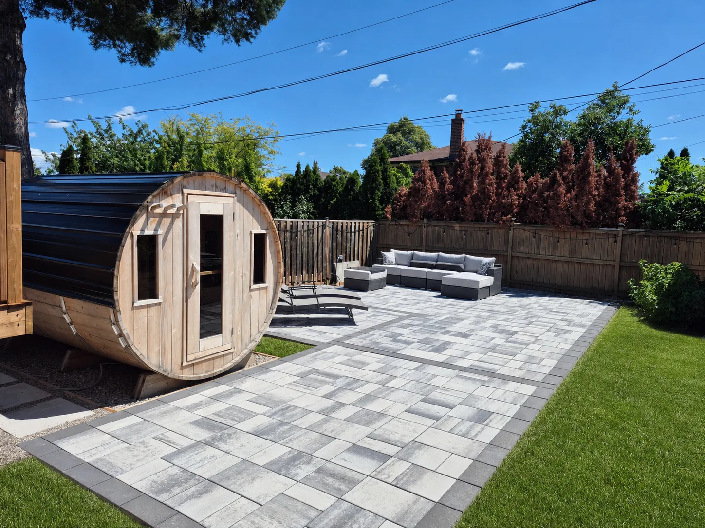 Backyard interlock patio with grey pavers, dark borders and outdoor seating; lawn digitally visualised.