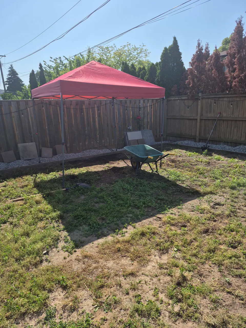 The backyard before interlock installation, with open ground, a canopy tent and materials along the fence.