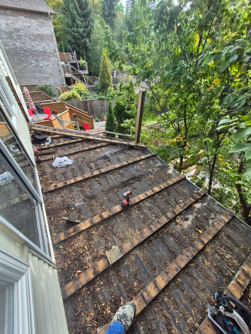 Upper deck with old boards removed, exposing the existing roof and supporting timber beside the house.