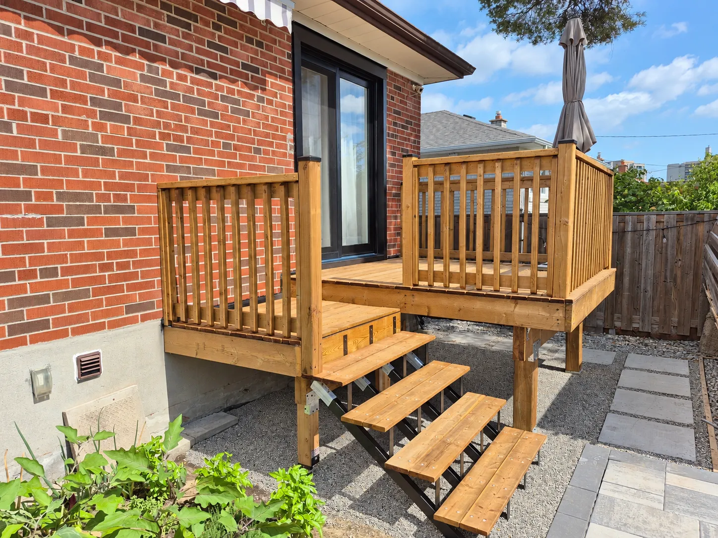New timber deck with railings and stairs beside a brick house.