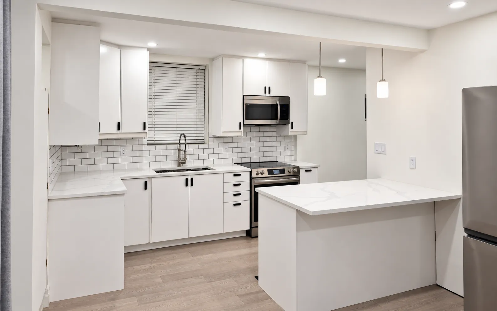 Renovated kitchen with white cabinets, tiled backsplash and pendant lighting.